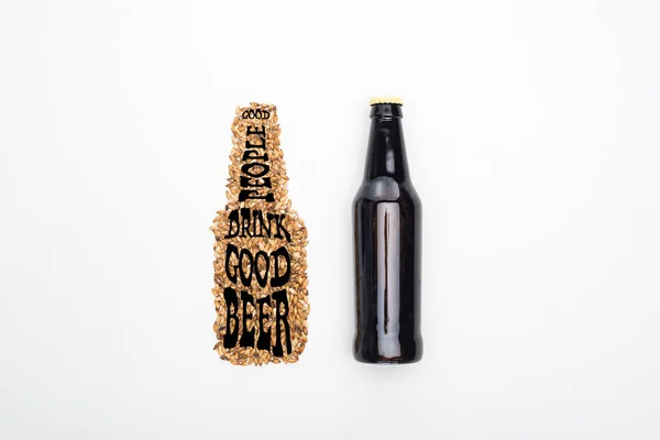 Vista dall'alto della bottiglia di birra leggera vicino ai chicchi di grano integrale con buone persone che bevono una buona scritta di birra isolata sul bianco — Foto stock