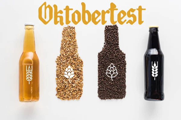 Vista superior de garrafas de cerveja escura e leve perto de grãos de trigo e café isolados em branco com letras Oktoberfest — Fotografia de Stock