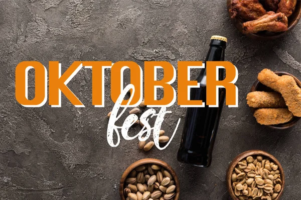 Draufsicht auf Flasche dunkles Bier in der Nähe von Schüsseln mit Snacks auf grauer Oberfläche mit Oktoberfest-Schriftzug — Stockfoto