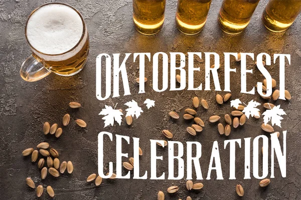 Vista superior de garrafas e vidro de cerveja leve perto de pistácios espalhados na superfície cinza com letras celebração Oktoberfest — Fotografia de Stock