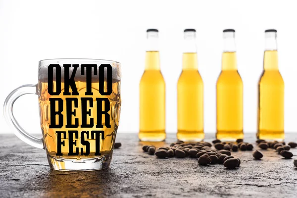 Selective focus of glass with light beer and oktebeer fest lettering near bottles and coffee grains isolated on white — Stock Photo