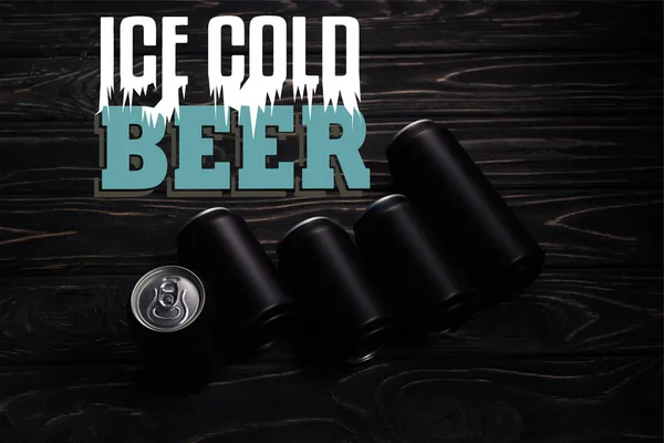 Black aluminum cans of beer on wooden table with ice cold beer lettering — Stock Photo