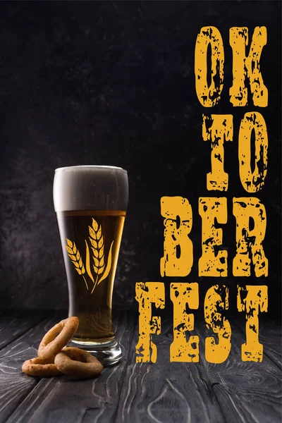 Glass of fresh light beer near fried onion rings on wooden table with yellow oktobeer fest lettering — Stock Photo