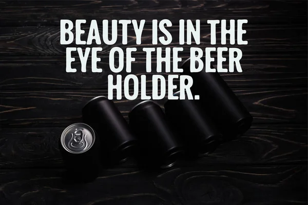 Black aluminum cans of beer on wooden table with beauty is in the eye of the beer holder illustration — Stock Photo