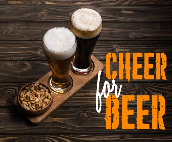 Glasses of dark and light beer near bowl with roasted peanuts on wooden table with cheer for beer lettering — Stock Photo