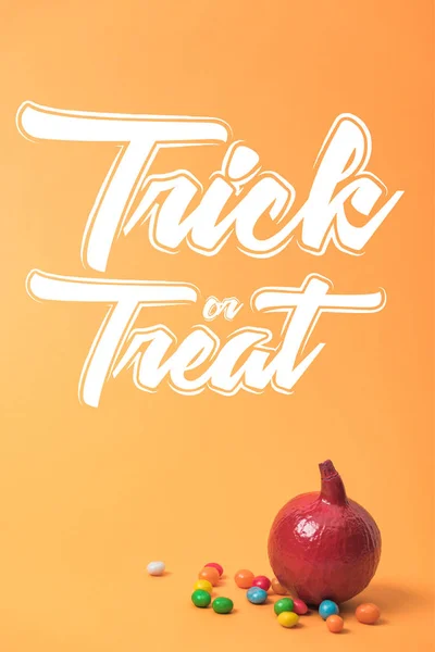 Bemalter roter Halloween-Kürbis mit Süßigkeiten auf orangefarbenem Hintergrund mit Trick oder Leckerli-Schriftzug — Stockfoto
