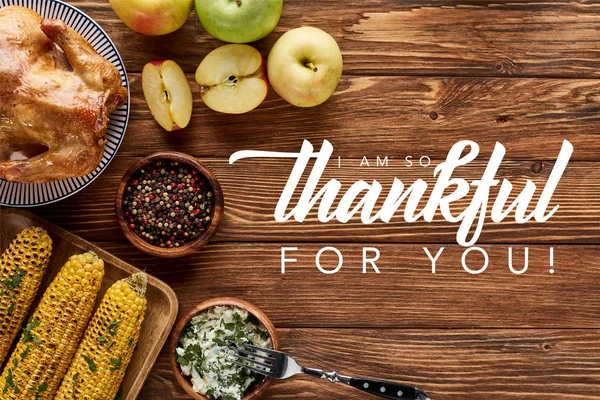 Top view of roasted turkey and grilled corn with apples served on wooden table with i am so thankful for you illustration — Stock Photo