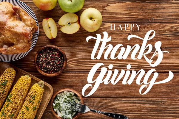 Vista superior de pavo asado y maíz a la parrilla con manzanas servidas en mesa de madera con feliz ilustración de acción de gracias - foto de stock