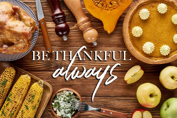Top view of roasted turkey, pumpkin pie and grilled vegetables served on wooden table with be thankful always illustration — Stock Photo