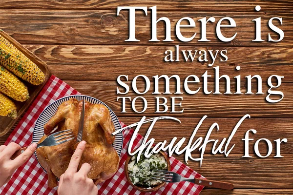 Cropped view of woman cutting roasted turkey on red plaid napkin near grilled corn on wooden table with there is always something to be thankful for lettering — Stock Photo