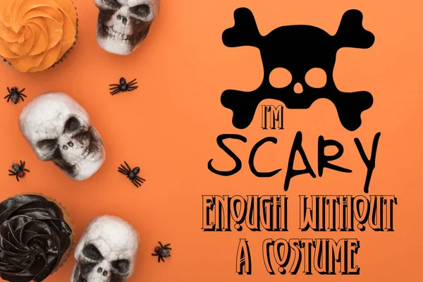 Top view of cupcakes, decorative skulls and spiders on orange background with i am scary enough without a costume illustration — Stock Photo