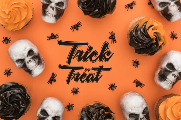 Vista superior de deliciosos cupcakes de Halloween con arañas y calaveras sobre fondo naranja con truco o ilustración de tratar - foto de stock