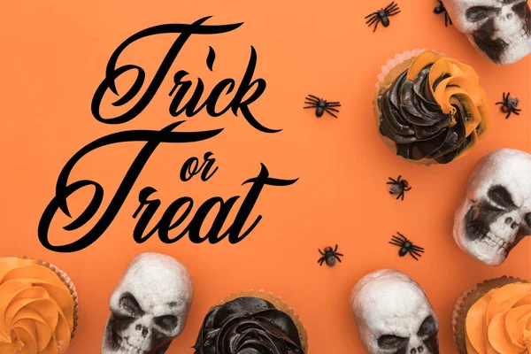 Vue du dessus de délicieux cupcakes d'Halloween avec des araignées et des crânes sur fond orange avec astuce ou traiter illustration — Photo de stock