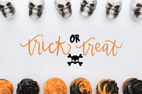 Draufsicht auf köstliche Halloween-Cupcakes und Totenköpfe auf weißem Hintergrund mit Trick oder Leckerbissen Illustration — Stockfoto