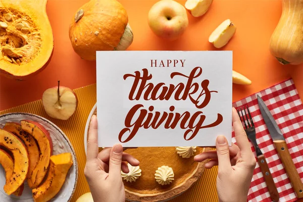 Vista recortada de la mujer que sostiene la tarjeta cerca con feliz pastel de calabaza ilustración de acción de gracias sobre fondo naranja - foto de stock