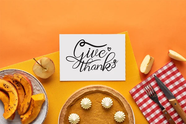 Vista superior de delicioso pastel de calabaza cerca de la tarjeta con dar gracias ilustración sobre fondo naranja con manzanas - foto de stock