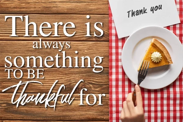 Vista recortada de la mujer comiendo pastel de calabaza en servilleta a cuadros con tarjeta de agradecimiento en la mesa de madera con siempre hay algo que agradecer por las letras - foto de stock