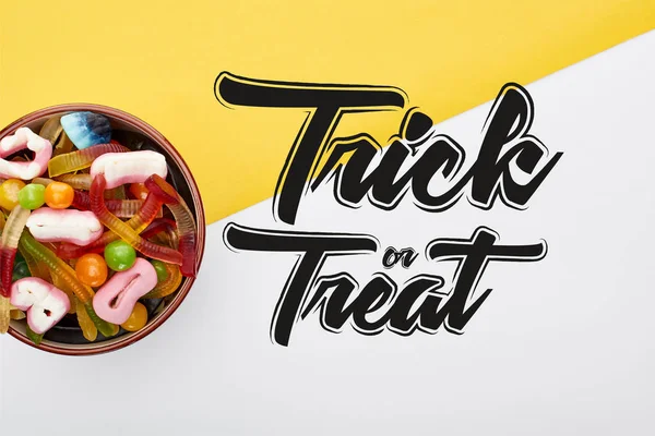 Vista superior de doces de goma coloridos em tigela no fundo amarelo e branco com truque ou ilustração tratar — Fotografia de Stock