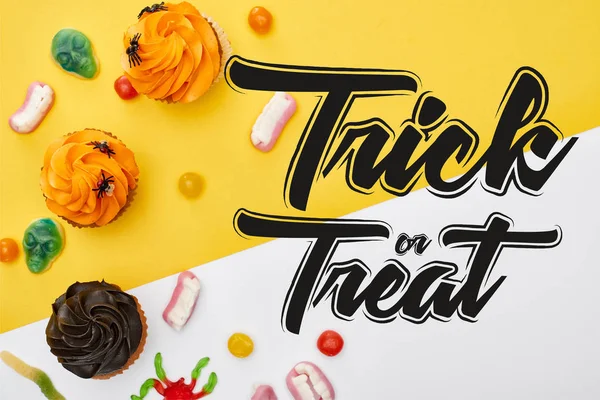 Top view of colorful gummy sweets and cupcakes on yellow and white background with trick or treat illustration — Stock Photo