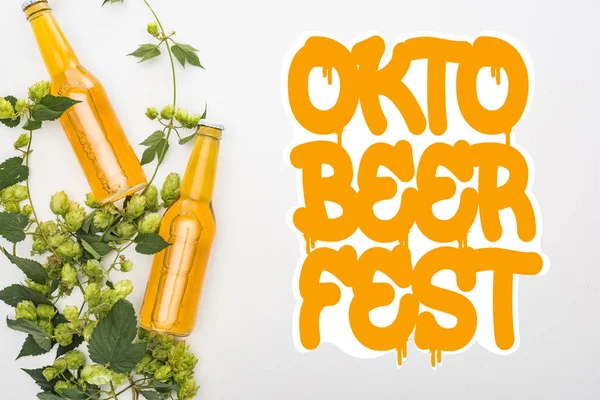 Vue du dessus de la bière en bouteilles avec houblon vert sur fond blanc avec lettrage Oktoberfest orange — Photo de stock