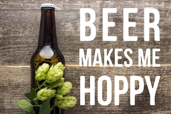 Top view of fresh beer in bottle with green hop on wooden surface with beer makes me hoppy illustration — Stock Photo