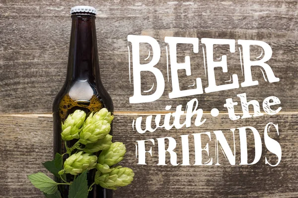 Vue du dessus de la bière fraîche en bouteille avec houblon vert sur la surface en bois avec de la bière avec les amis lettrage — Photo de stock