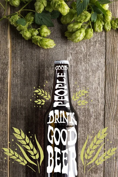 Top view of fresh beer in bottle with good people drink good beer lettering near green hop on wooden surface — Stock Photo