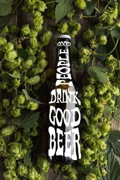 Top view of fresh beer in bottle with good people drink good beer lettering in green hop on wooden surface — Stock Photo