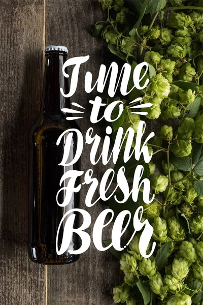 Top view of fresh beer in bottle with green hop on wooden surface with time to drink fresh beer illustration — Stock Photo