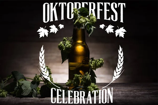 Свежее пиво в бутылке с зеленым хмелем на деревянной поверхности в темноте с белой иллюстрацией праздника Октоберфест — стоковое фото