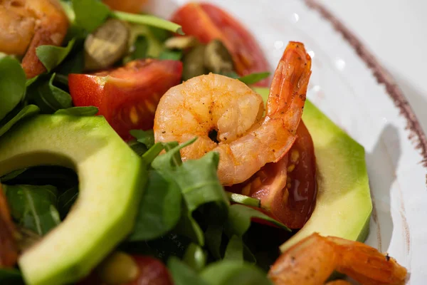 Nahaufnahme von frischem grünem Salat mit Kürbiskernen, Kirschtomaten, Garnelen und Avocado auf Teller — Stockfoto