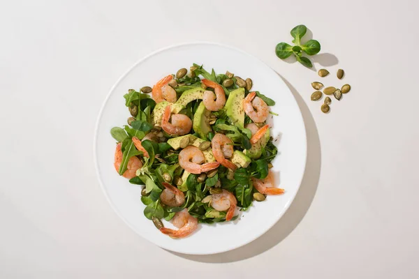 Draufsicht auf frischen grünen Salat mit Kürbiskernen, Garnelen und Avocado auf Teller auf weißem Hintergrund — Stockfoto