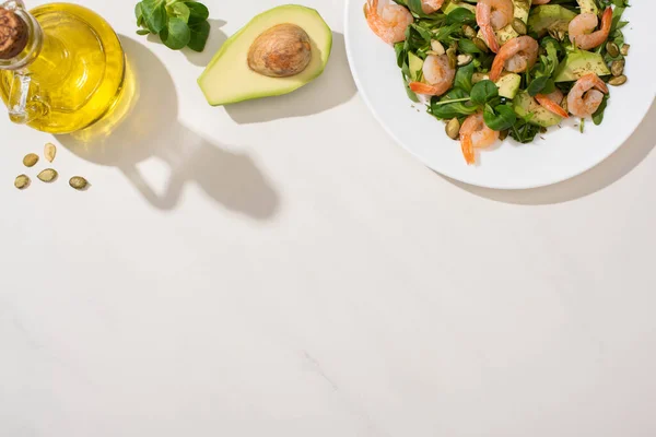 Vista dall'alto di insalata verde fresca con semi di zucca, gamberetti e avocado sul piatto vicino agli ingredienti su sfondo bianco — Foto stock