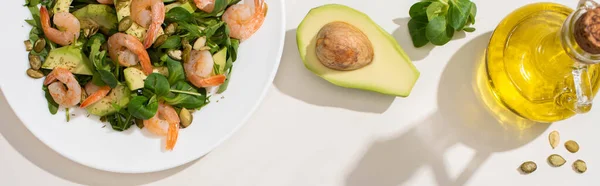 Vue du dessus de la salade verte fraîche avec des graines de citrouille, crevettes et avocat sur l'assiette près des ingrédients sur fond blanc, image horizontale — Photo de stock