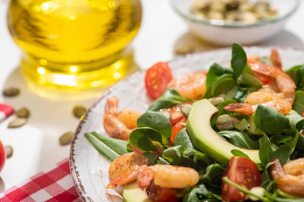 Foco seletivo de salada verde fresca com camarões e abacate na placa e guardanapo xadrez no fundo branco — Fotografia de Stock