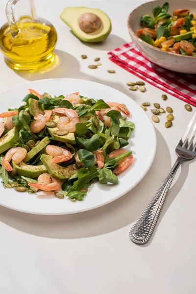 Selective focus of fresh green salad with shrimps and avocado on plates near fork and oil — Stock Photo