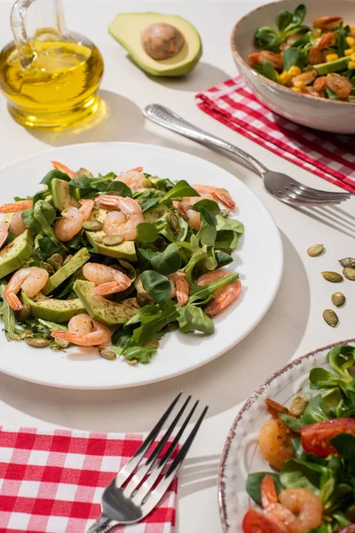 Enfoque selectivo de ensalada verde fresca con camarones y aguacate en platos cerca de tenedores y aceite - foto de stock