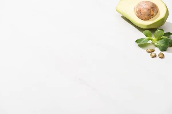 Avocado verde fresco, foglie verdi e semi di zucca su sfondo bianco — Foto stock
