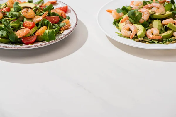 Ensalada verde fresca con camarones y aguacate en platos sobre fondo blanco - foto de stock