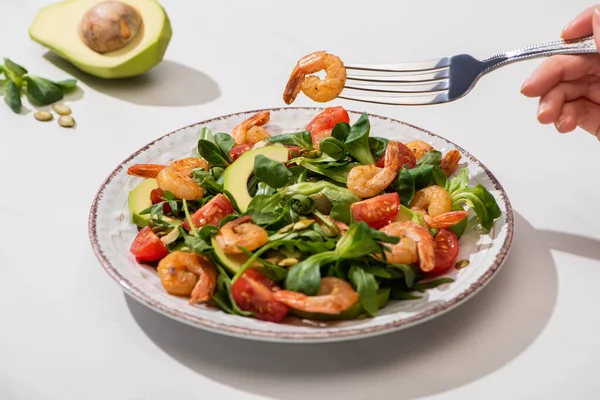 Teilansicht einer Frau, die frischen grünen Salat mit Kirschtomaten, Garnelen und Avocado auf weißem Hintergrund isst — Stockfoto