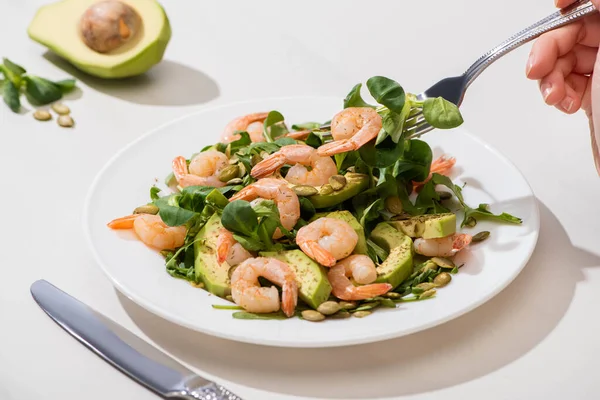 Vue partielle de la femme mangeant de la salade verte fraîche avec des graines de citrouille, des crevettes et de l'avocat sur fond blanc — Photo de stock