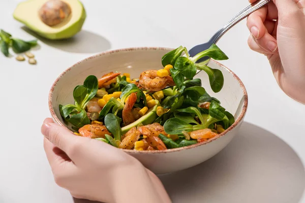 Partial view of woman eating fresh green salad with corn, shrimps and avocado on white background — Stock Photo