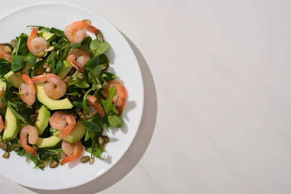 Draufsicht auf frischen grünen Salat mit Kürbiskernen, Garnelen und Avocado auf Teller auf weißem Hintergrund — Stockfoto