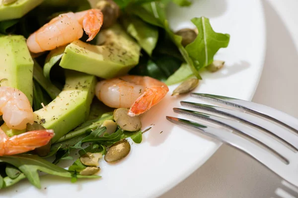 Close up view of fresh green salad with pumpkin seeds, shrimps and avocado on plate with fork — Stock Photo