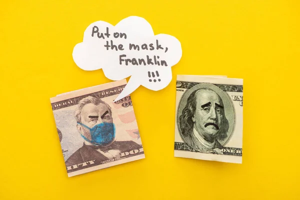 Vista superior de los billetes con máscara médica dibujada y expresiones faciales cerca de la burbuja del habla sobre fondo amarillo - foto de stock