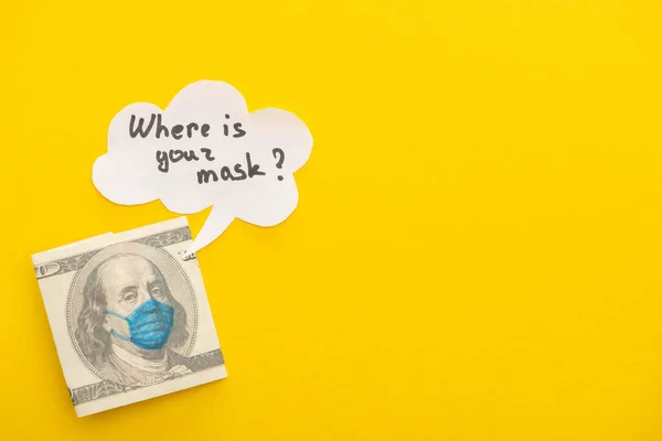 Vista superior del billete de dólar con máscara médica dibujada y burbuja del habla sobre fondo amarillo - foto de stock