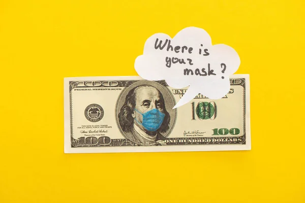 KYIV, UCRANIA - 25 DE MARZO DE 2020: vista superior del billete en dólares con máscara médica dibujada y burbuja del habla sobre fondo amarillo - foto de stock