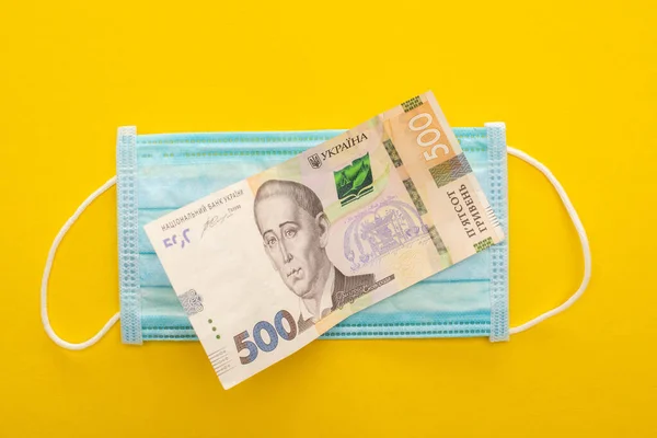 Vista dall'alto della banconota ucraina e maschera medica su sfondo giallo — Foto stock