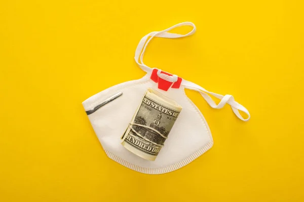 Vista superior do rolo de dinheiro e máscara de segurança no fundo amarelo — Fotografia de Stock