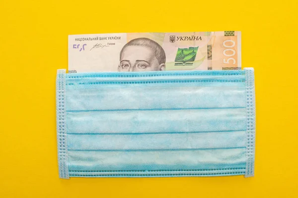 Vue du haut du billet ukrainien et masque médical sur fond jaune — Photo de stock